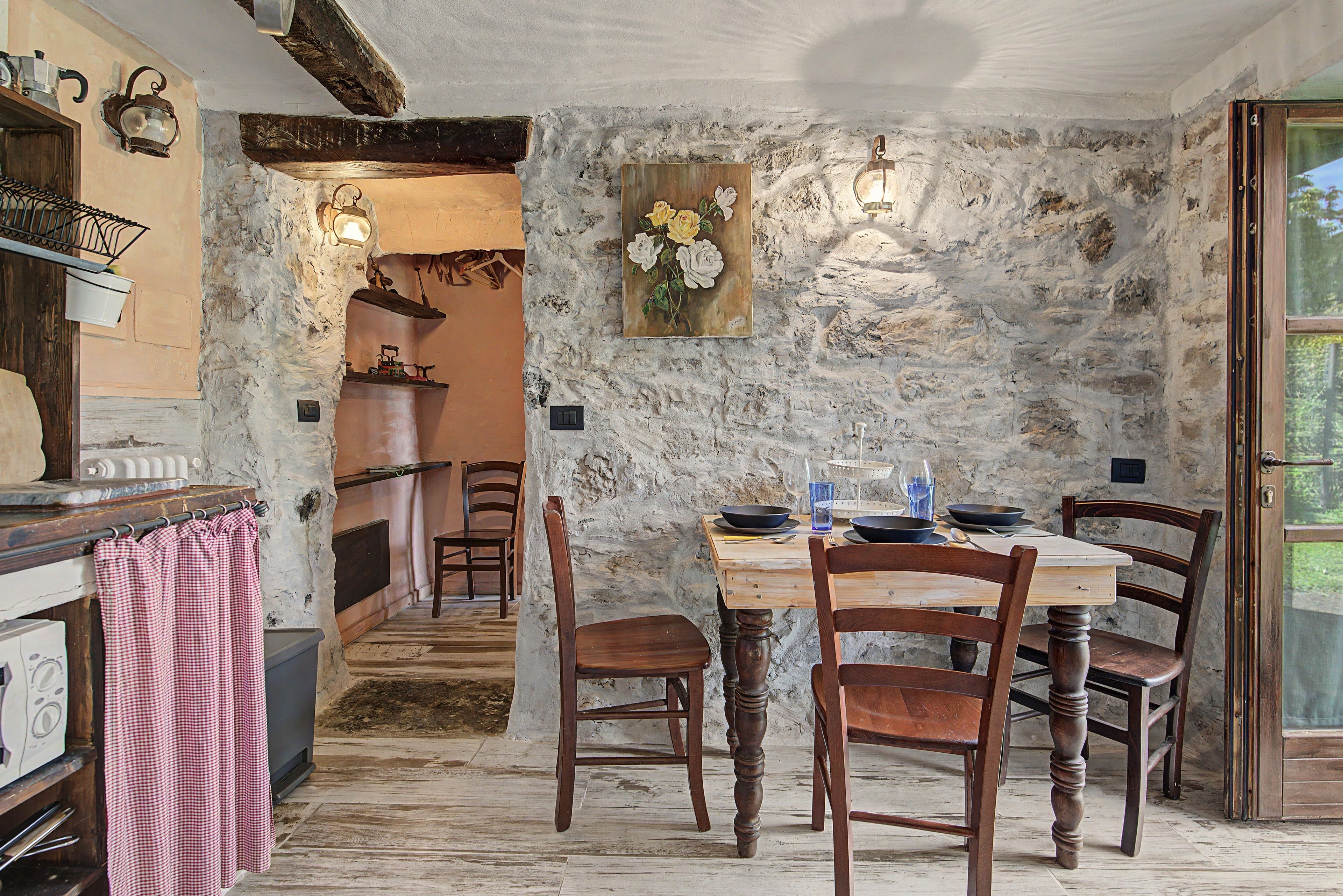 A rustic dining area with a stone wall, wooden furniture, and a view of the kitchen.
