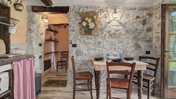 A rustic dining area with a stone wall, wooden furniture, and a view of the kitchen.