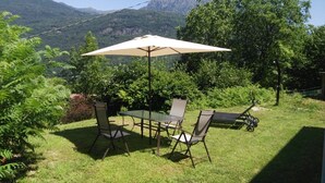 Une terrasse avec une table et des chaises, un parasol et une vue sur les montagnes.