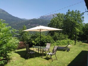 Une terrasse avec une table et des chaises, un parasol et une vue sur les montagnes.