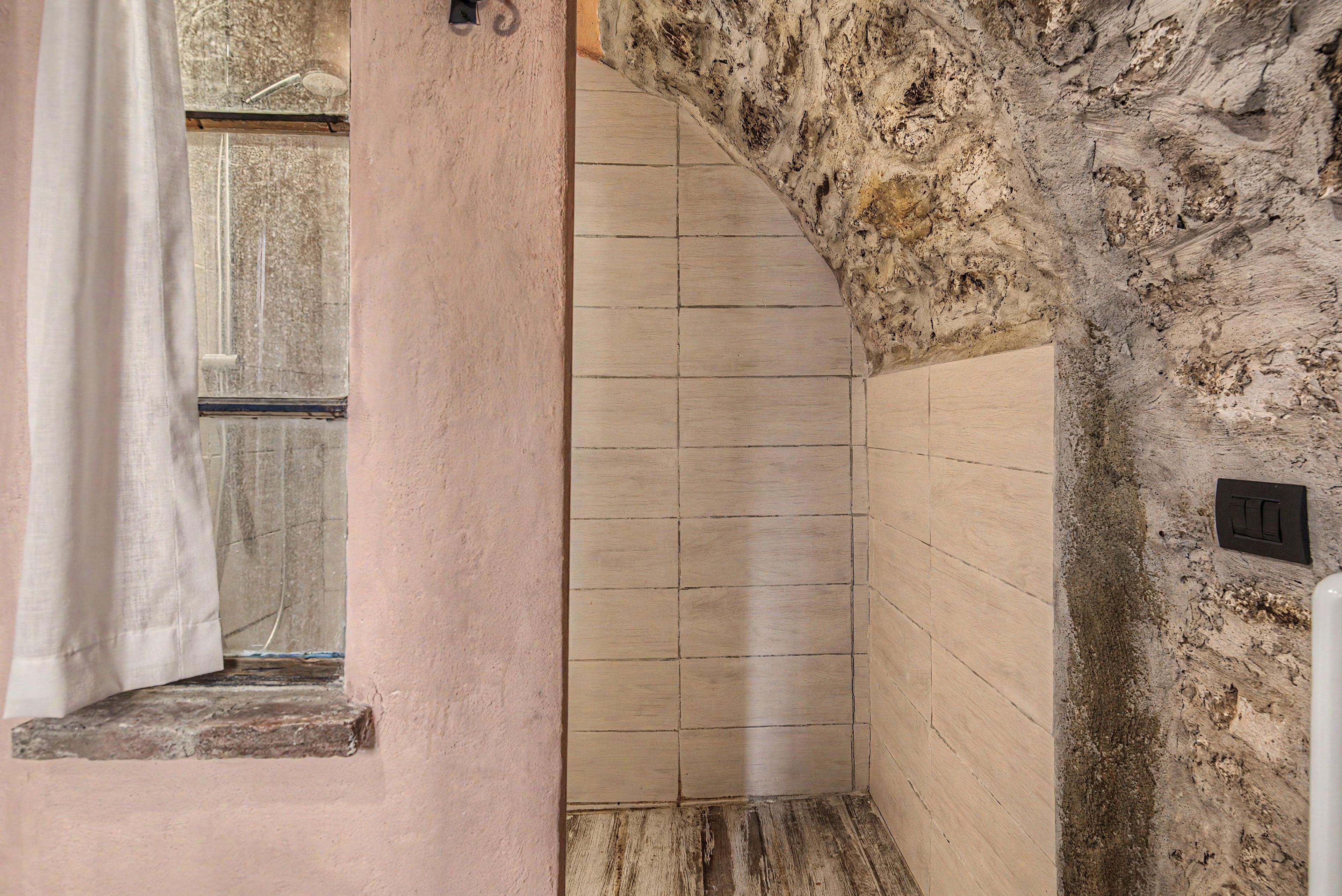 A bathroom with a stone wall, a window with a curtain, and a tiled floor.