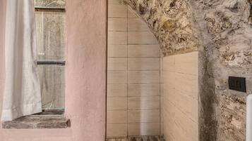 A bathroom with a stone wall, a window with a curtain, and a tiled floor.