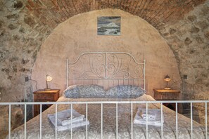 Ein Schlafzimmer mit Steinwand, einem Bett mit Metallkopfteil, zwei Nachttischen mit Lampen und einem Gemälde über dem Bett.