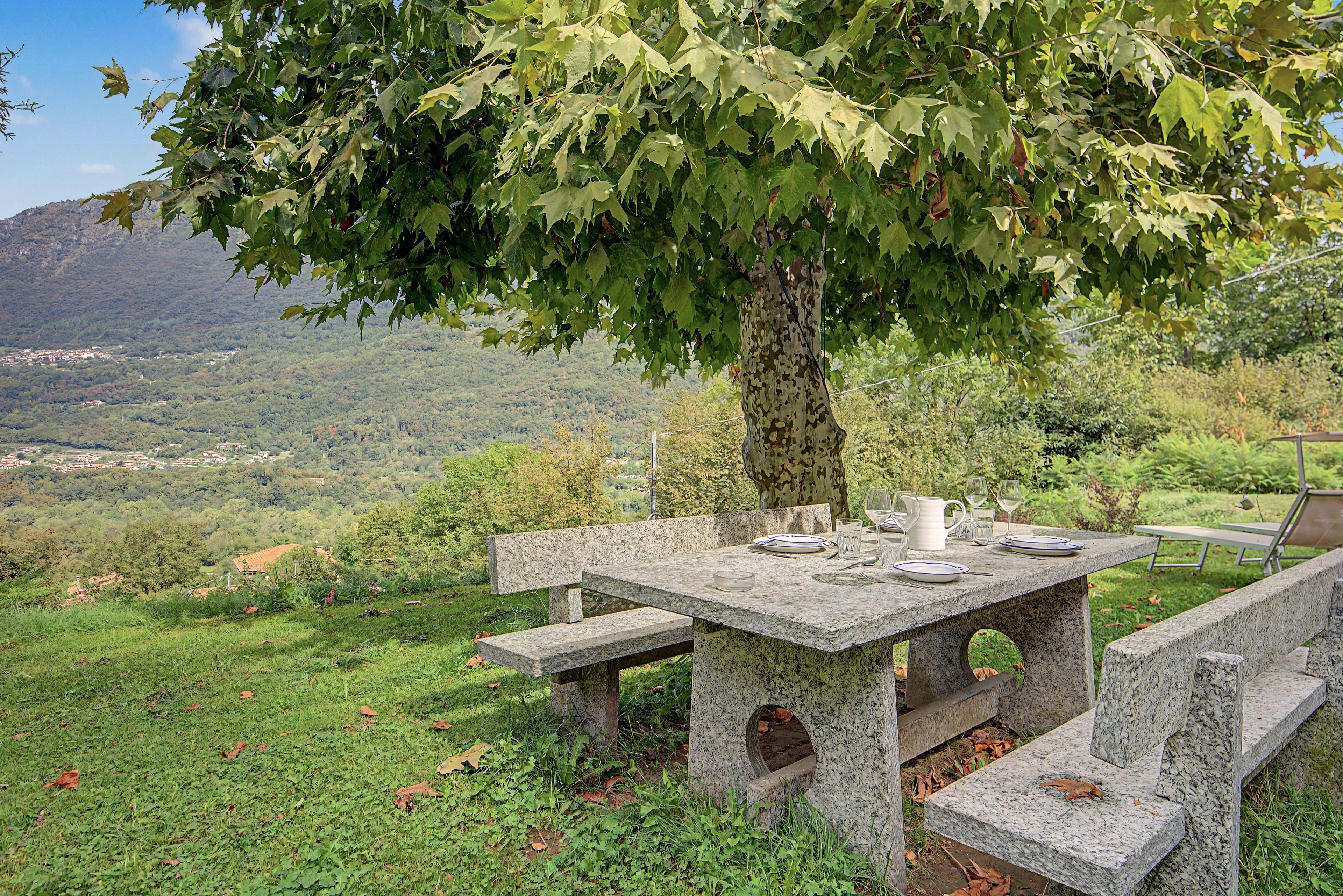 An outdoor stone table with benches, set against a backdrop of a mountainous landscape.