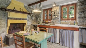 Une cuisine rustique avec un mur en pierre, des poutres en bois, un four encastré et une fenêtre donnant sur un paysage verdoyant.