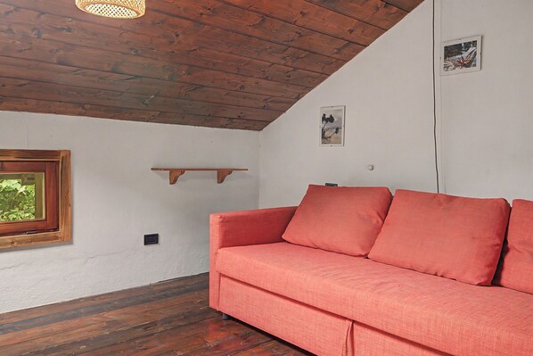 Una habitación con techo de madera, un sofá rojo, una ventana con vistas a la vegetación y un estante pequeño en la pared.