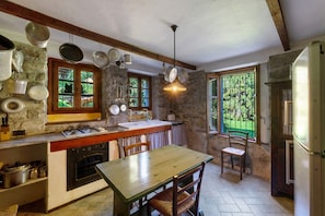 A rustic kitchen with stone walls, wooden beams, a wooden table, and a hanging pot rack.