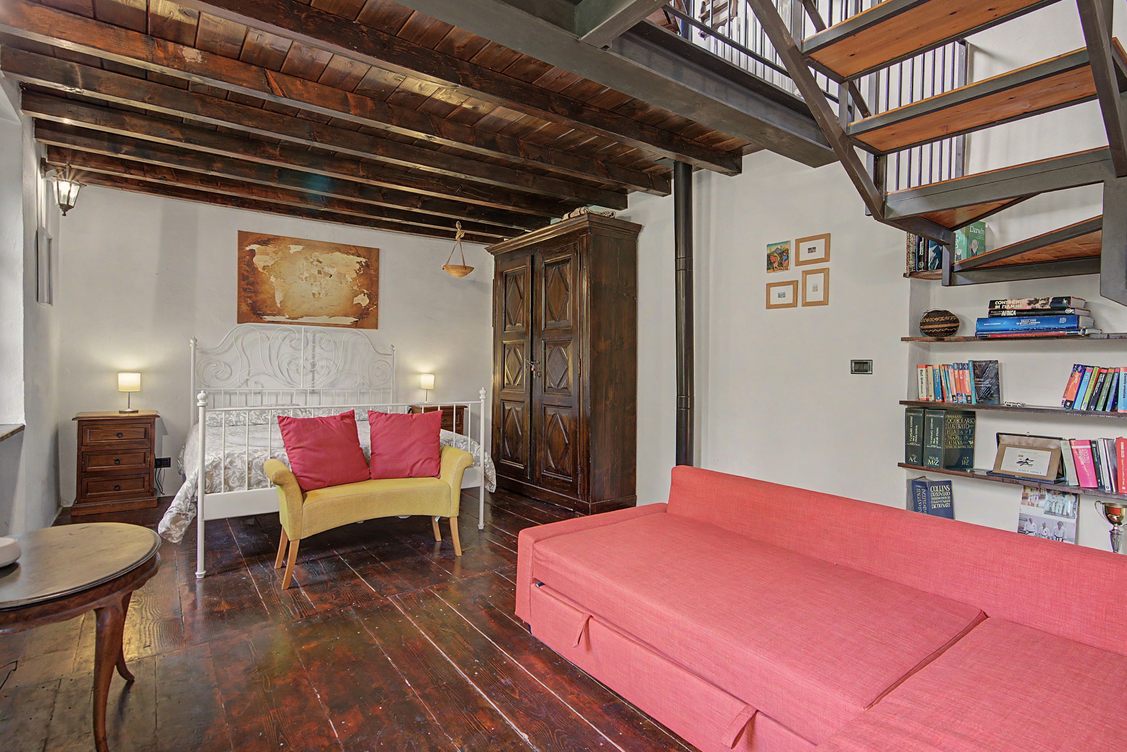 A room with a bed, a red sofa, a wooden cabinet, and a bookshelf with books.