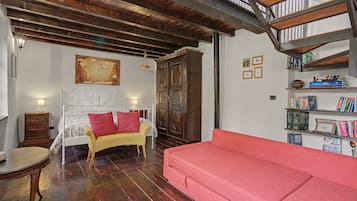 A room with a bed, a red sofa, a wooden cabinet, and a bookshelf with books.