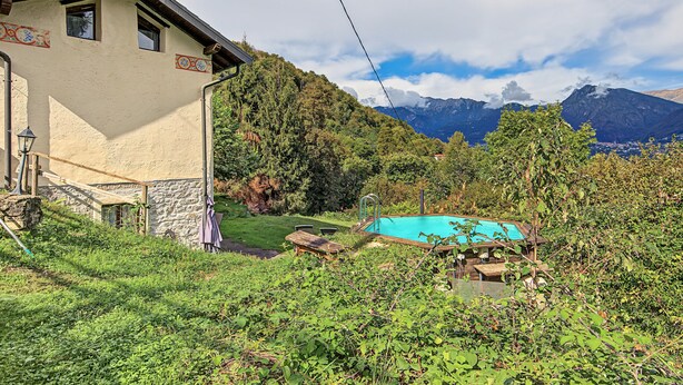 Une maison avec un mur en pierre, une terrasse en bois et une piscine entourée de verdure.