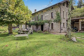 A stone building with a garden, outdoor seating, and a motorcycle parked outside.