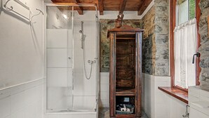 Une salle de bain avec une douche à parois de verre, un meuble en bois et un mur en pierre.