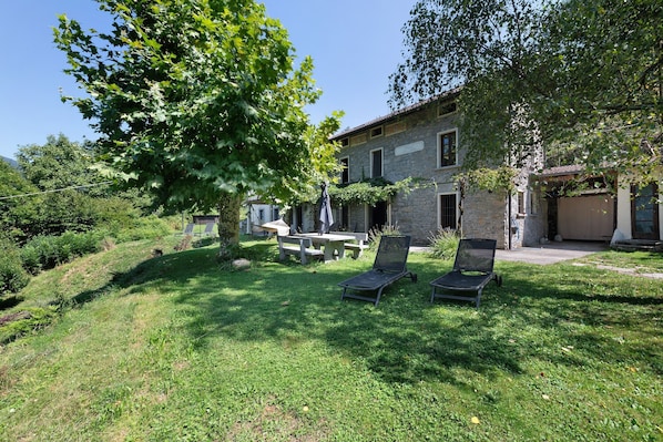 A stone building with a grassy yard, two lounge chairs, and a picnic table.