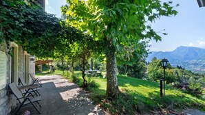 Ein gepflasterter Weg führt zu Sitzgelegenheiten im Freien, einer Pergola und einer Aussicht auf ein Gebirge.