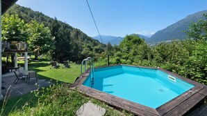 Ein rechteckiger Pool mit Holzterrasse, umgeben von üppigem Garten und Bergblick.