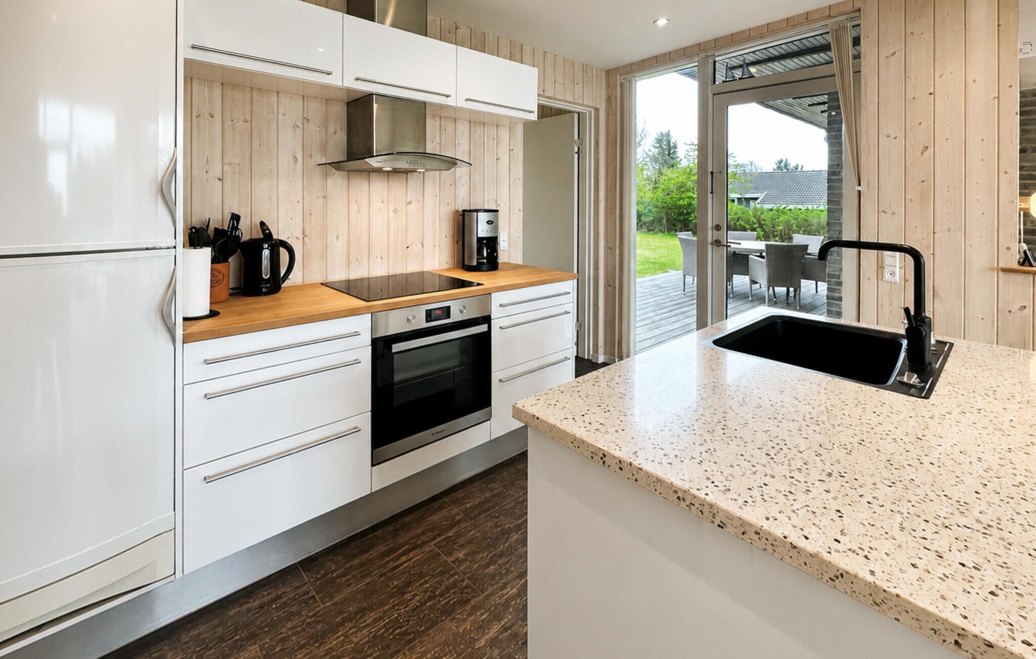 A modern kitchen with white cabinets, a wooden countertop, a stainless steel range hood, and a large window.