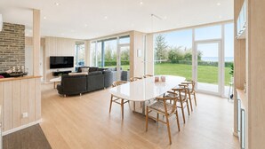 A modern kitchen with a TV, a dining area with a large table and chairs, and a view of the outdoors. - Beach front home in Spøttrup (Spøttrup)