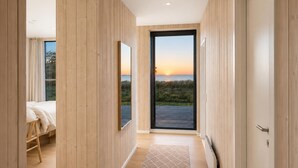 A modern hotel room with a wooden interior, a large sliding glass door leading to a balcony with a view of the sunset. - Beach front home in Spøttrup (Spøttrup)