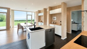 A modern kitchen with a dishwasher, a dining area with a table and chairs, and a view of the outdoors. - Beach front home in Spøttrup (Spøttrup)