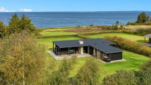 A modern house with a large deck, a well-maintained lawn, and a view of the sea. - Beach front home in Spøttrup (Spøttrup)