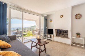 Een woonkamer met een bank, een tafel, een open haard en een balkon met tuinmeubilair.