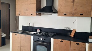A kitchen with wooden cabinets, a stove, oven, and a black range hood. - Apartment 'Batsi View House' with Sea View, Wi-Fi and Air Conditioning (Andros)