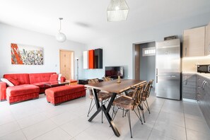 Una sala de estar moderna con un sofá rojo, una mesa de comedor de madera y una zona de cocina con refrigerador.