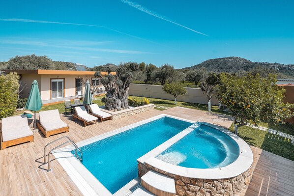 Una piscina con sillas de descanso y sombrillas, rodeada por una terraza de madera y muros de piedra.