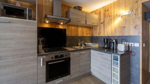 A compact kitchen with wooden paneling, a built-in microwave, a stove, and a sink. - Apartment 'Arc 2000' with Mountain View and Balcony (Bourg-Saint-Maurice)