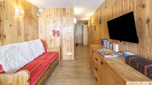 A wooden interior with a sofa, a flat-screen TV, and a counter with various items. - Apartment 'Arc 2000' with Mountain View and Balcony (Bourg-Saint-Maurice)