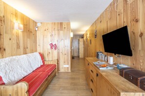 A wooden interior with a sofa, a flat-screen TV, and a counter with various items. - Apartment 'Arc 2000' with Mountain View and Balcony (Bourg-Saint-Maurice)