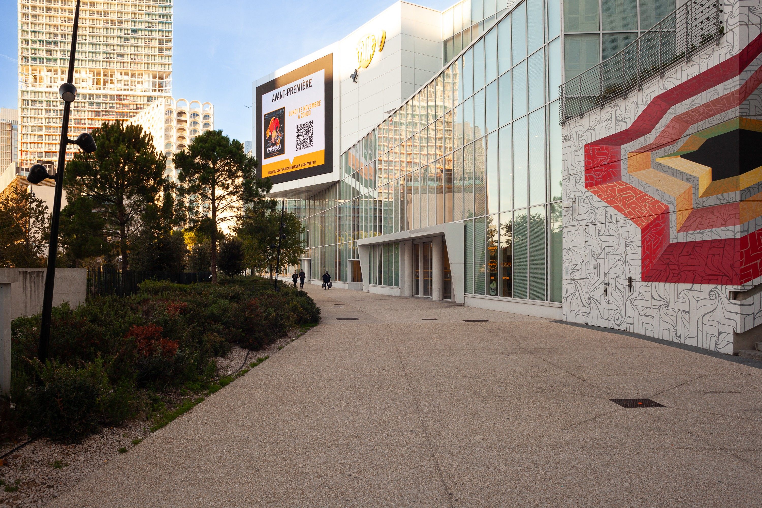 Un bâtiment moderne doté d’une façade en verre et d’une grande fresque murale extérieure.