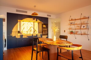 A modern kitchen with a central island, a dining table with chairs, and a wall-mounted shelf with decorative items. - Apartment "Porte Bleue" with Sea View, Private Terrace & Wi-Fi (Marseille)