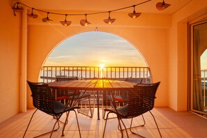 A terrace with a table and chairs, a railing, and a view of the sunset over the water. - Apartment "Porte Bleue" with Sea View, Private Terrace & Wi-Fi (Marseille)