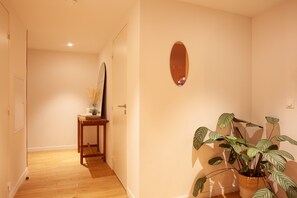 A hallway with a wooden floor, a door, a small table with a vase and candles, and a potted plant.