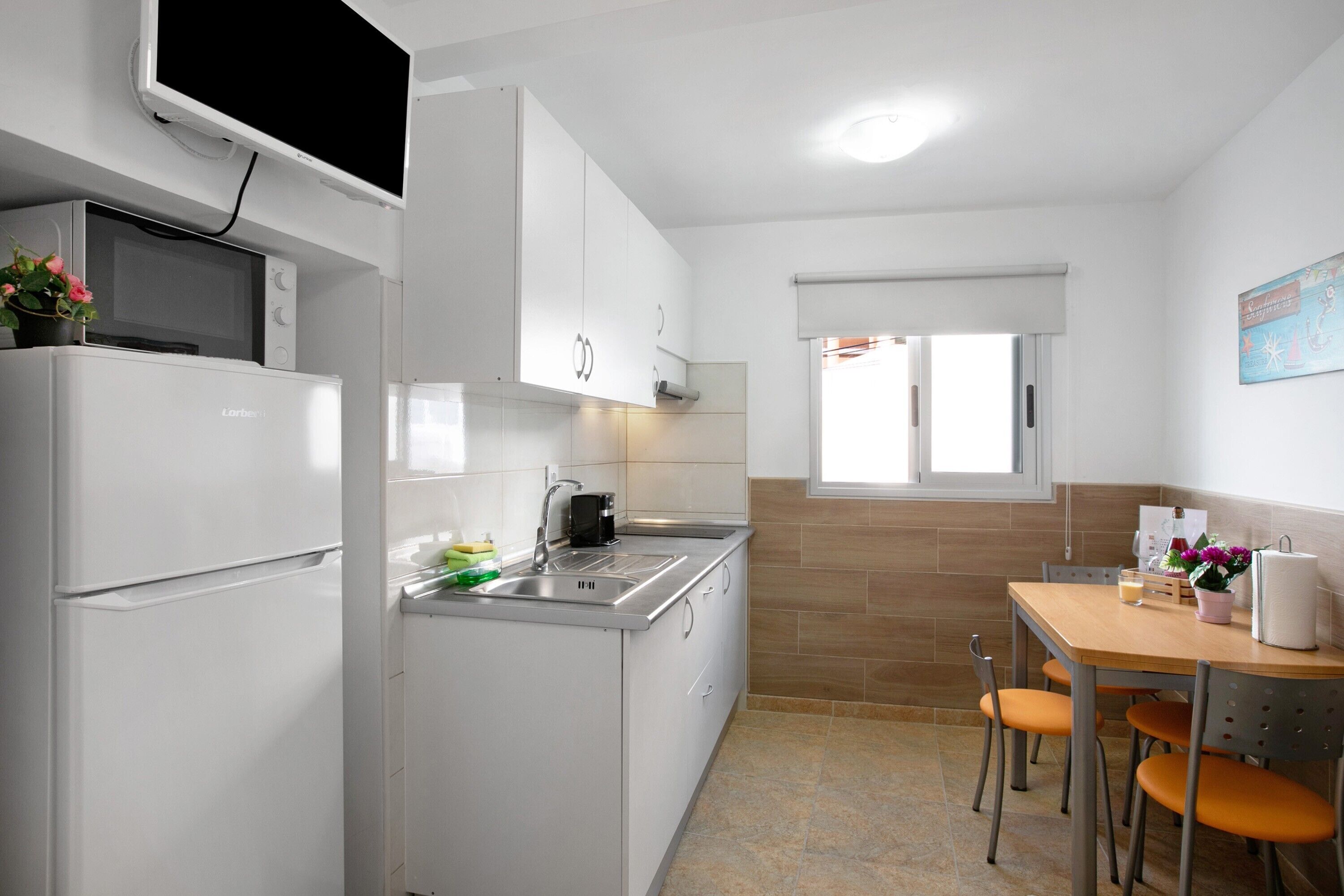 Een kleine keuken met een magnetron, fornuis, spoelbak en een eethoek met tafel en stoelen.