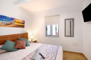 Habitación de hotel con cama, almohadas, un cuadro, ventana, espejo y televisor.