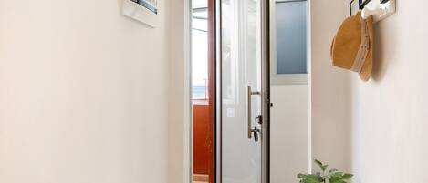 Un pasillo con puerta de vidrio, una planta en maceta y un sombrero colgado en la pared.