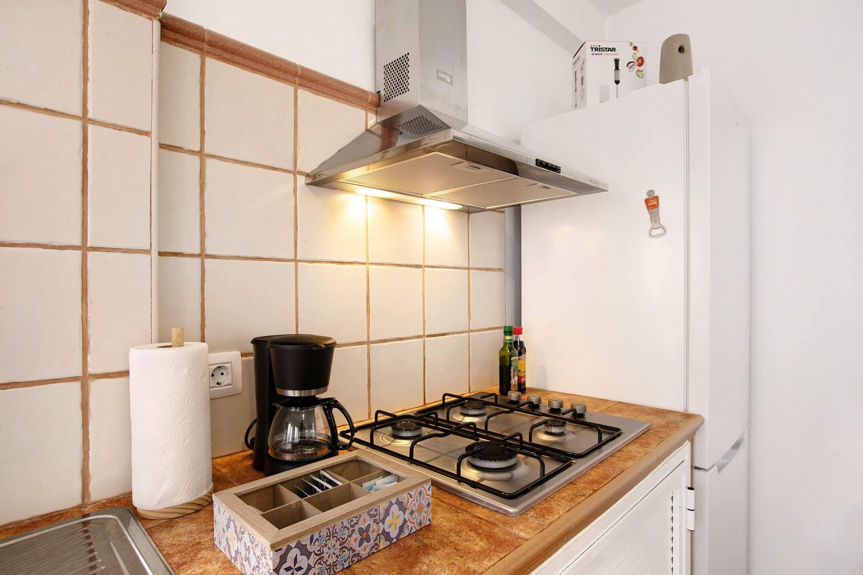 A kitchen with a gas stove, a coffee maker, a paper towel holder, and a box of utensils.