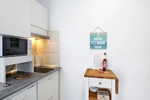 Una cocina con microondas, una mesa de madera con un cartel y una botella de vino.