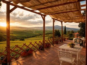 Eine überdachte Terrasse mit Blick auf sanfte Hügel und einen Sonnenuntergang.