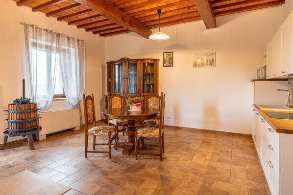 A dining area with a wooden table and chairs, a cabinet with glass doors, and a kitchen area with cabinets and a sink. - Apartment "Agriturismo Il Casato Mag-il Torchio" with Mountain Views, Terrace and Wi-Fi (Pienza)