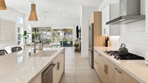 Une cuisine moderne dotée d’un îlot central, d’appareils électroménagers en acier inoxydable et donnant sur le patio extérieur.