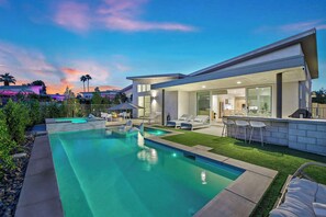 Una casa moderna con piscina, mobiliario exterior y césped bien cuidado.