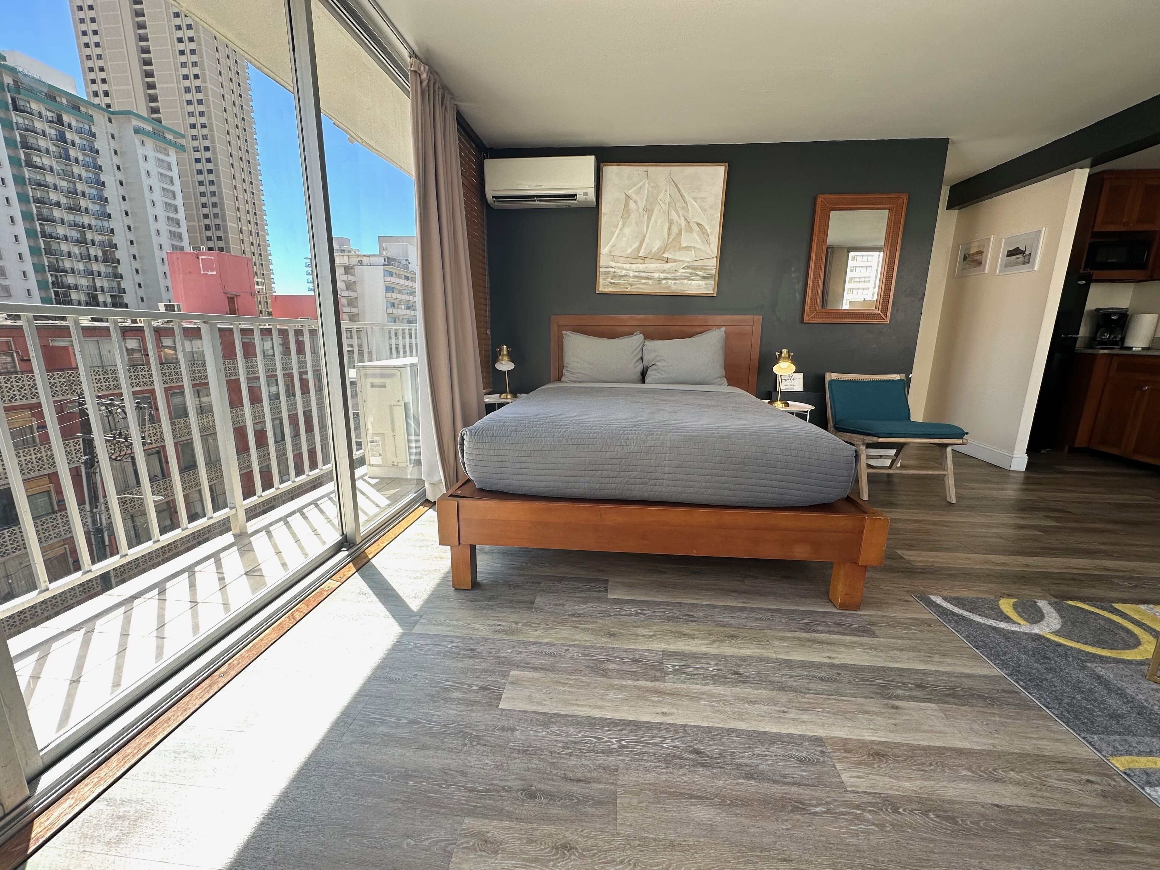 Habitación de hotel con una cama grande, un escritorio pequeño, una silla, un balcón con barandilla y vistas a edificios altos.