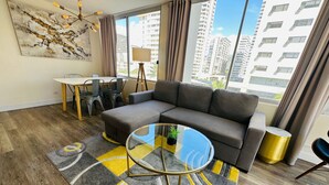 A modern living room with a sectional sofa, a glass coffee table, and a dining area with chairs and a table. - Contemporary Waikiki Beach Condo with Rooftop Pool, Superb Shopping and Dinning  (Honolulu)