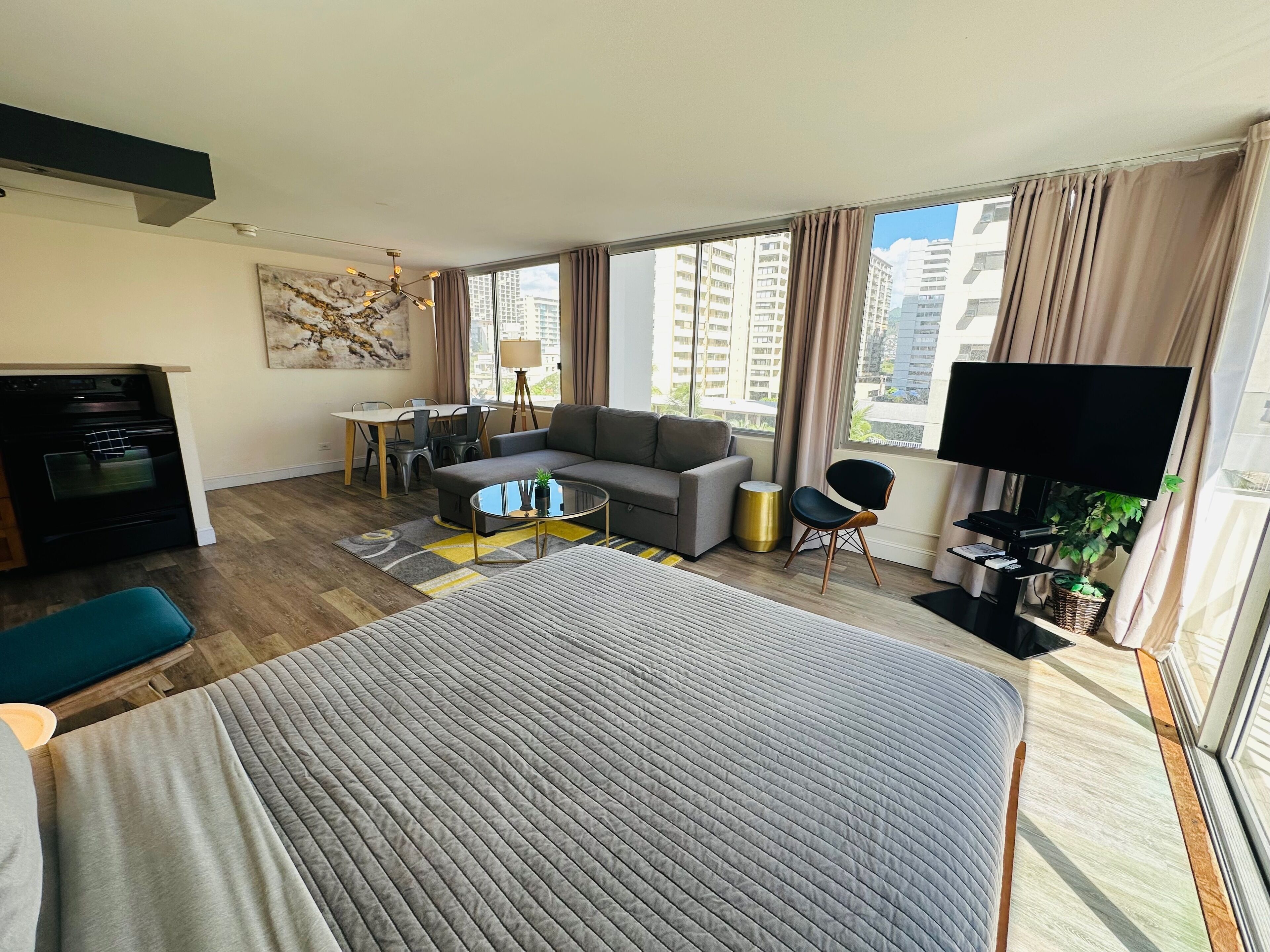 A modern hotel room with a large bed, a sofa, a dining table, and a TV.
