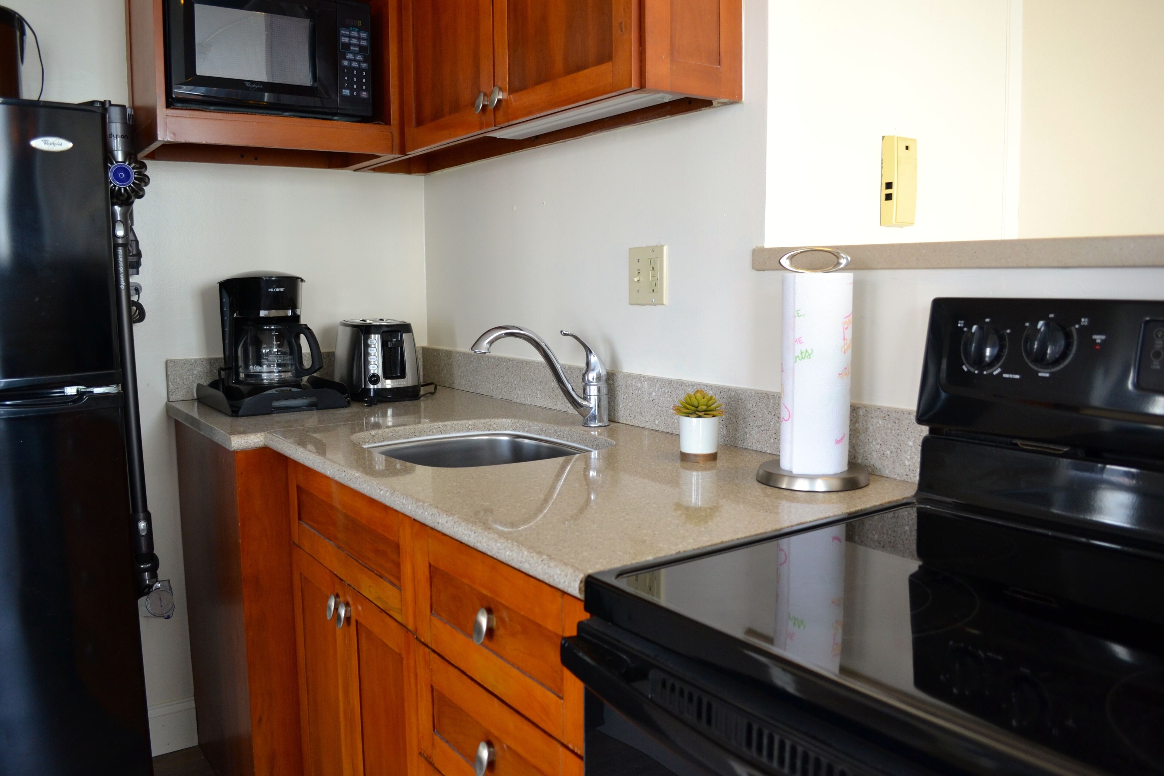 A kitchen with wooden cabinets, a stainless steel sink, a black stove, a microwave, and a coffee maker.