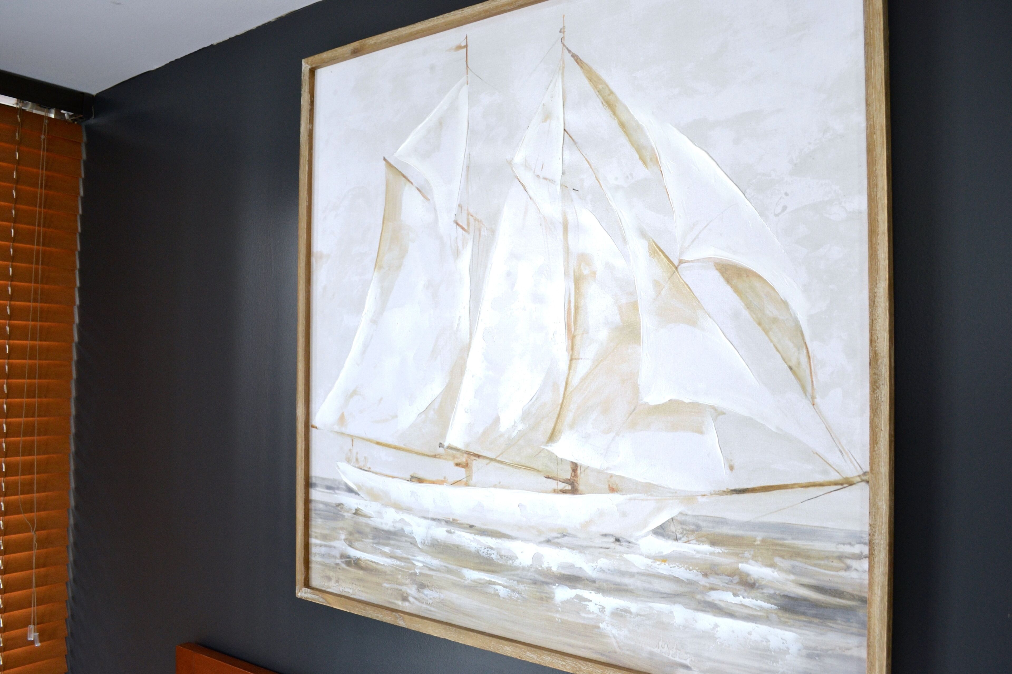 Una obra de arte enmarcada que muestra un velero en un mar tranquilo, colgada en una pared oscura.