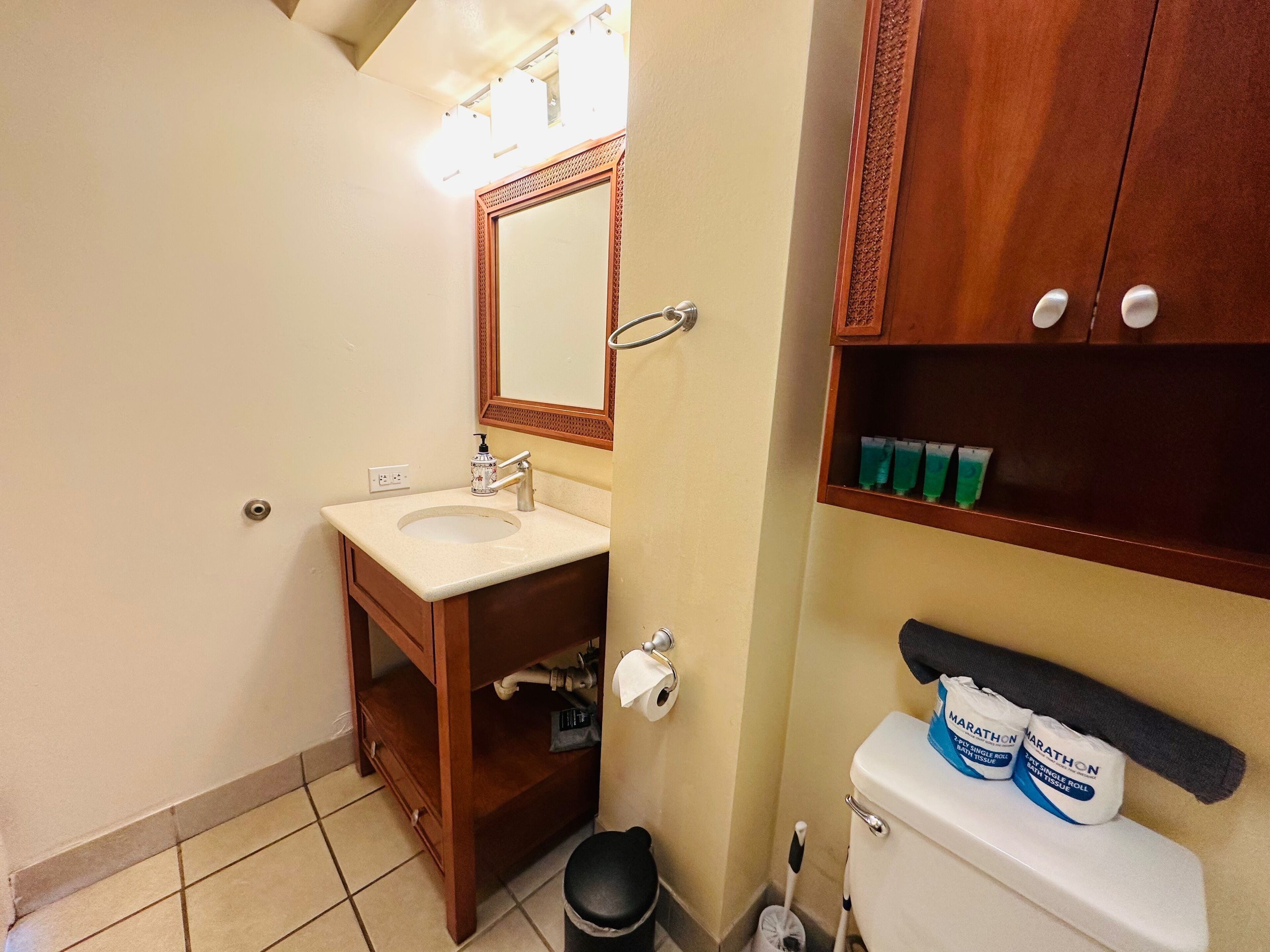 A bathroom with a sink, mirror, toilet, and storage shelves.